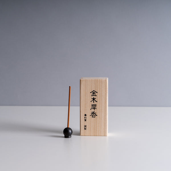 Kousaido incense stick paired with a spherical holder, presented next to a wooden box inscribed with Japanese kanji, against a minimalist grey background.