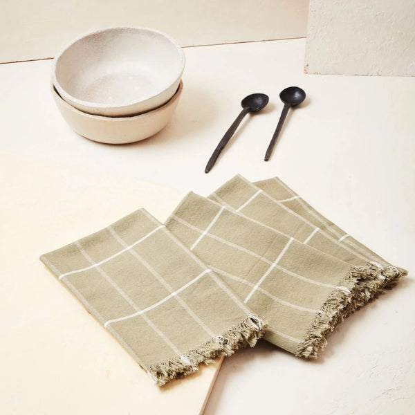 Four green sage napkins on a table with two bowls and two spoons on the side