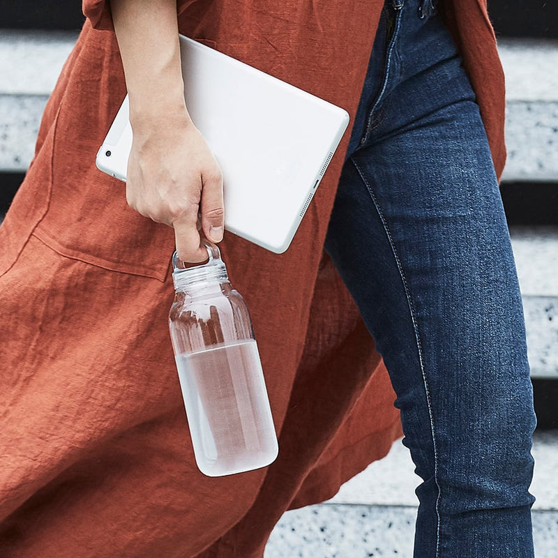 A person holding a Kinto Water Bottle in Clear while walking.