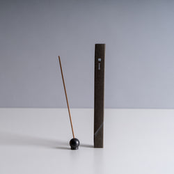 Brown Waboku incense stick resting on a black spherical holder, with minimalist packaging in the background.
