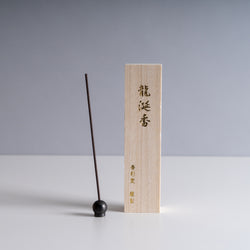 Ambergris Incense Stick beside a light wooden box with Japanese calligraphy on a minimalist background.