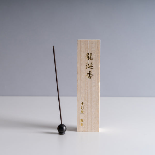 Ambergris Incense Stick beside a light wooden box with Japanese calligraphy on a minimalist background.