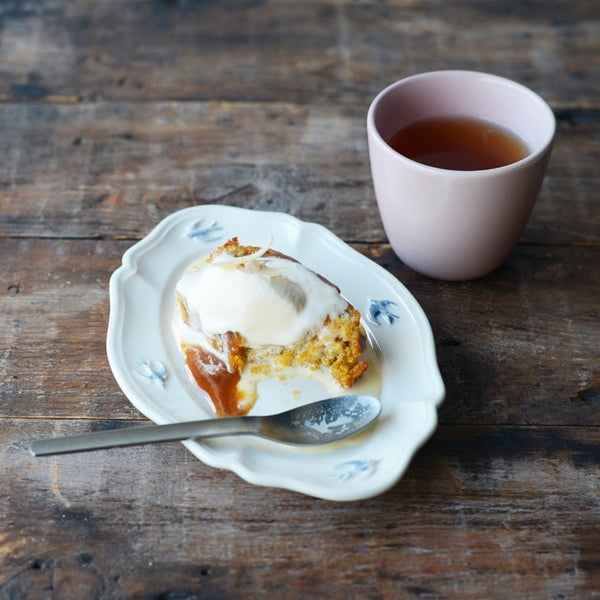 A cake on the 7.5" Studio M' early bird oval plate next to a cup of tea on a wooden table 