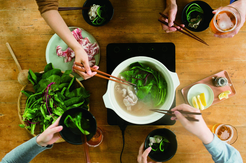 Birds-eye view of a group of people cooking nabe in a Kinto 2.5L KAKOMI IH Donabe in White