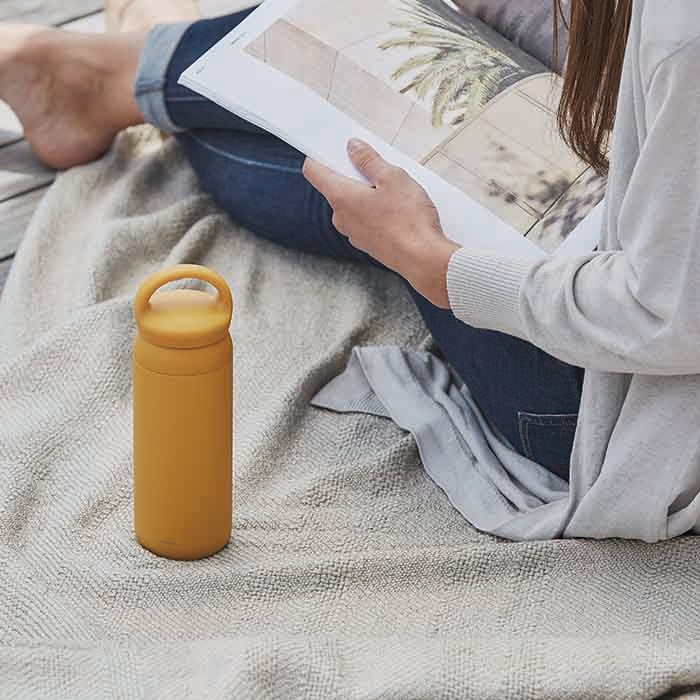 A person reading a book with a Kinto Day Off Tumbler in Mustard