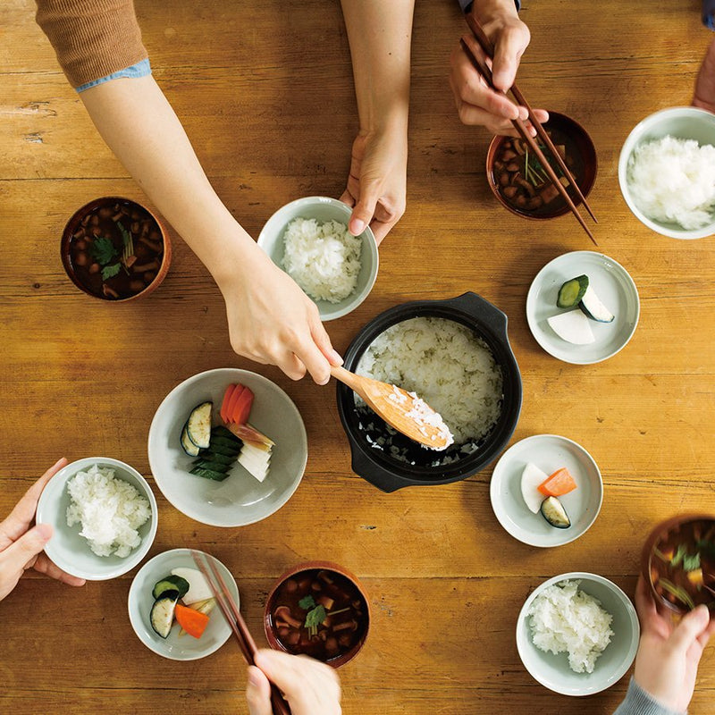 Birds-eye view of a dinning table with cooked white rice in a Kinto KAKOMI Rice Cooker in Black, and some ceramic side plates and rice bowls